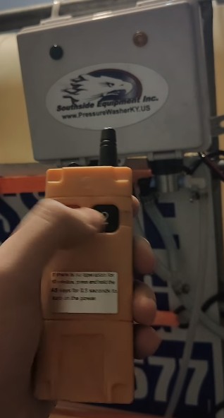 Hand holding orange remote near industrial control box