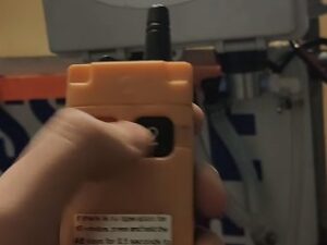 Hand holding orange remote controller near machine
